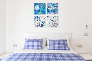 A bed with a blue and white checkered bedspread and pillows, a white headboard, and four abstract art pieces on the wall.