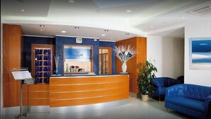 A hotel reception area with a wooden reception desk, a blue sofa, and a large painting on the wall.