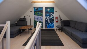 Un dormitorio estilo loft moderno con tragaluces, un ventanal grande, un sofá, una mesita y un cuadro en la pared.