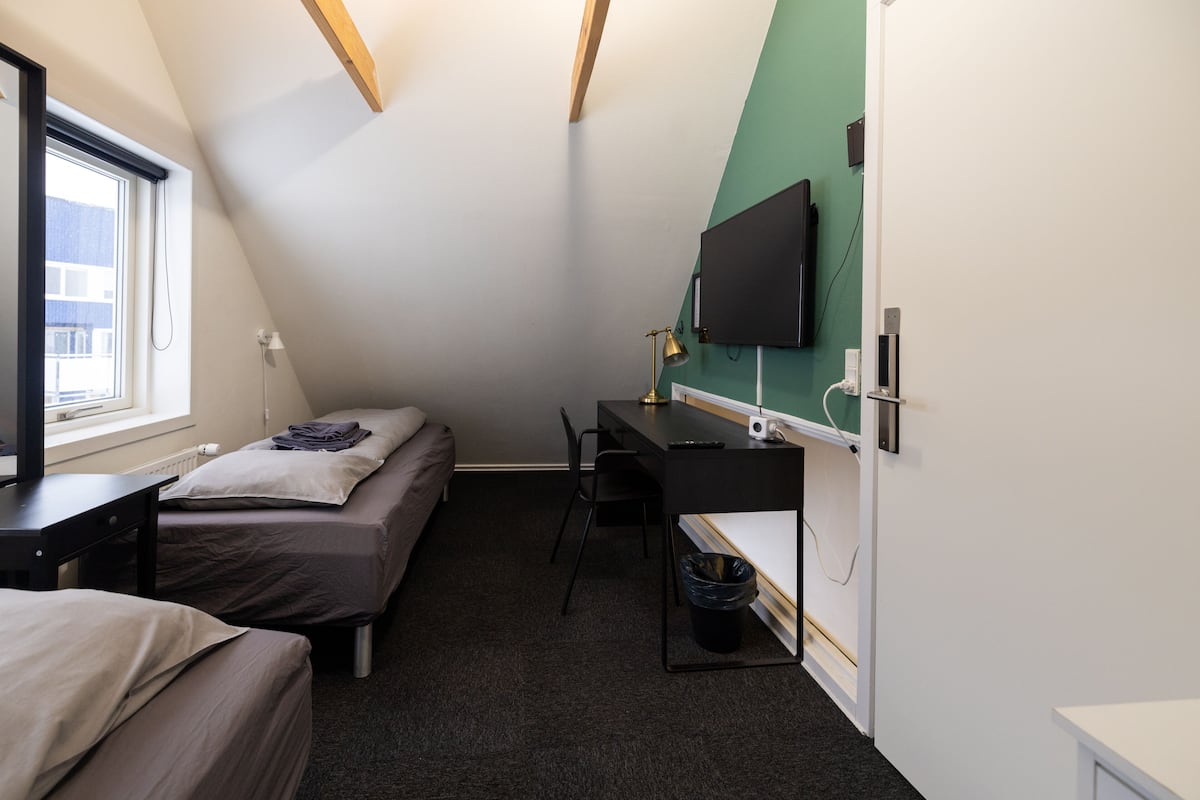 A small, well-lit room with a bed, a desk, and a television mounted on the wall.