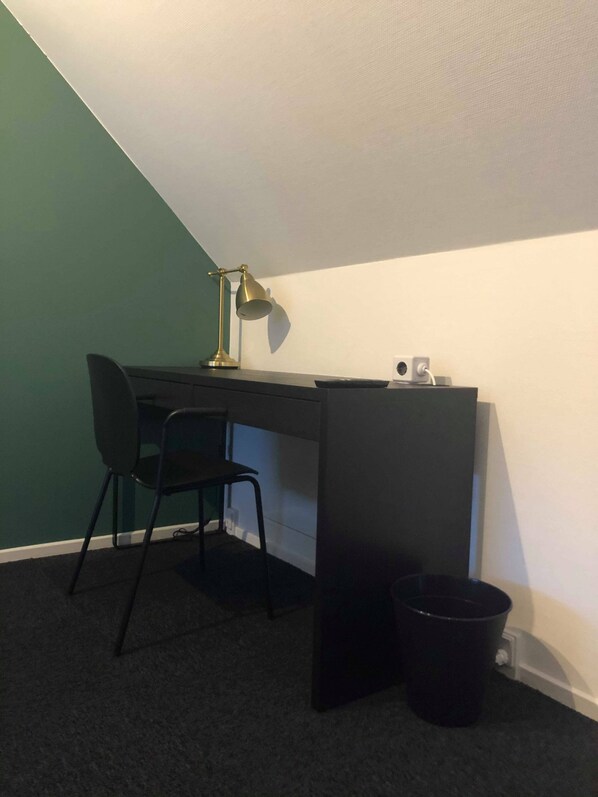 A small, dark-colored desk with a chair and a lamp in a corner.