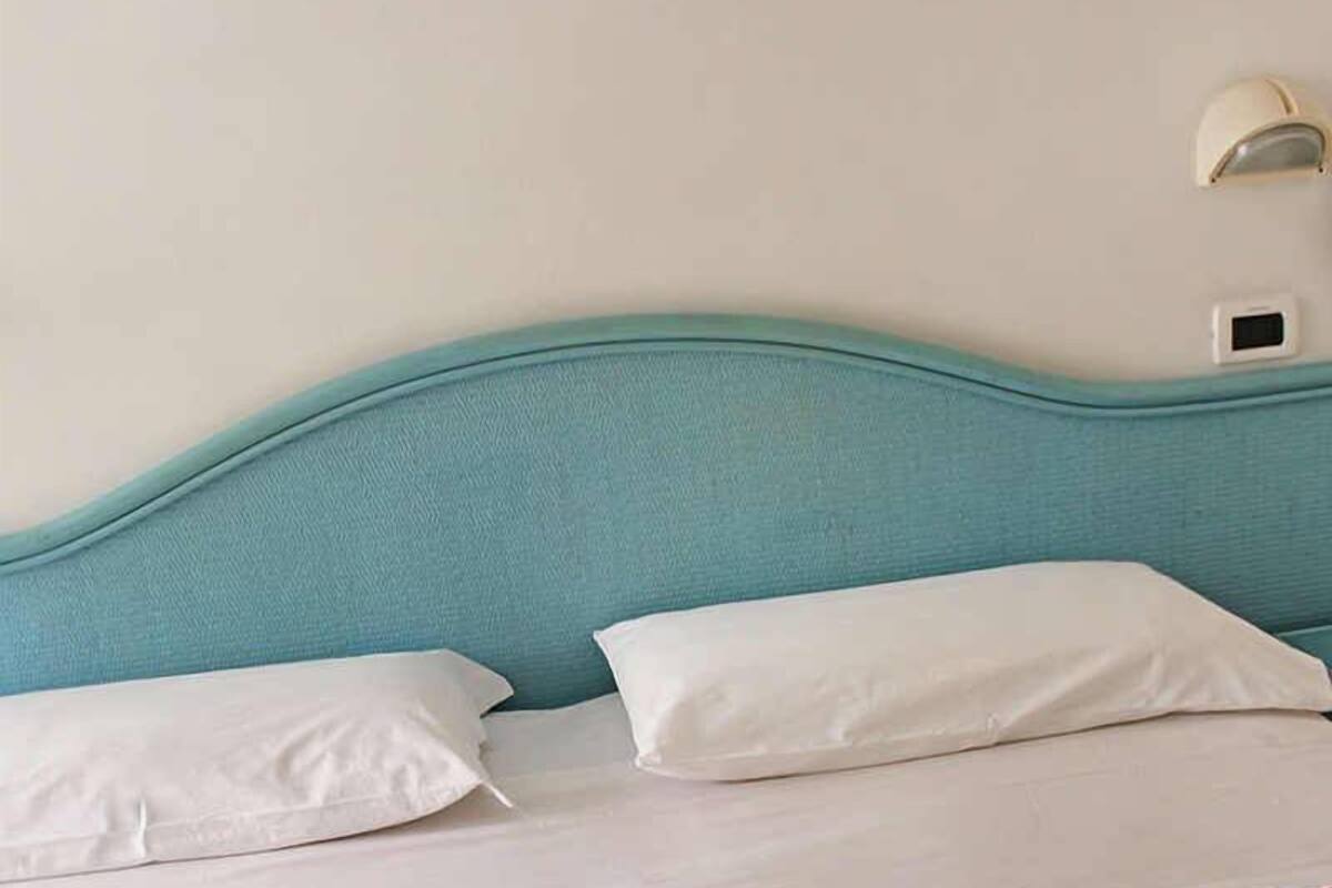 Una cama con ropa blanca y un cabecero verde azulado.
