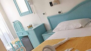 Ett hotellrum med en säng, ett skrivbord, en stol, en spegel och ett litet bord.