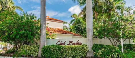 A building with a sign reading 'Club Bahia' surrounded by lush greenery and palm trees.
