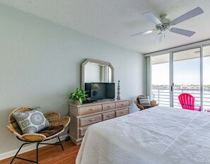 Ein Schlafzimmer mit einem Bett, einem Schminktisch, einem Fernseher, einem Deckenventilator und einem großen Fenster mit Aussicht.