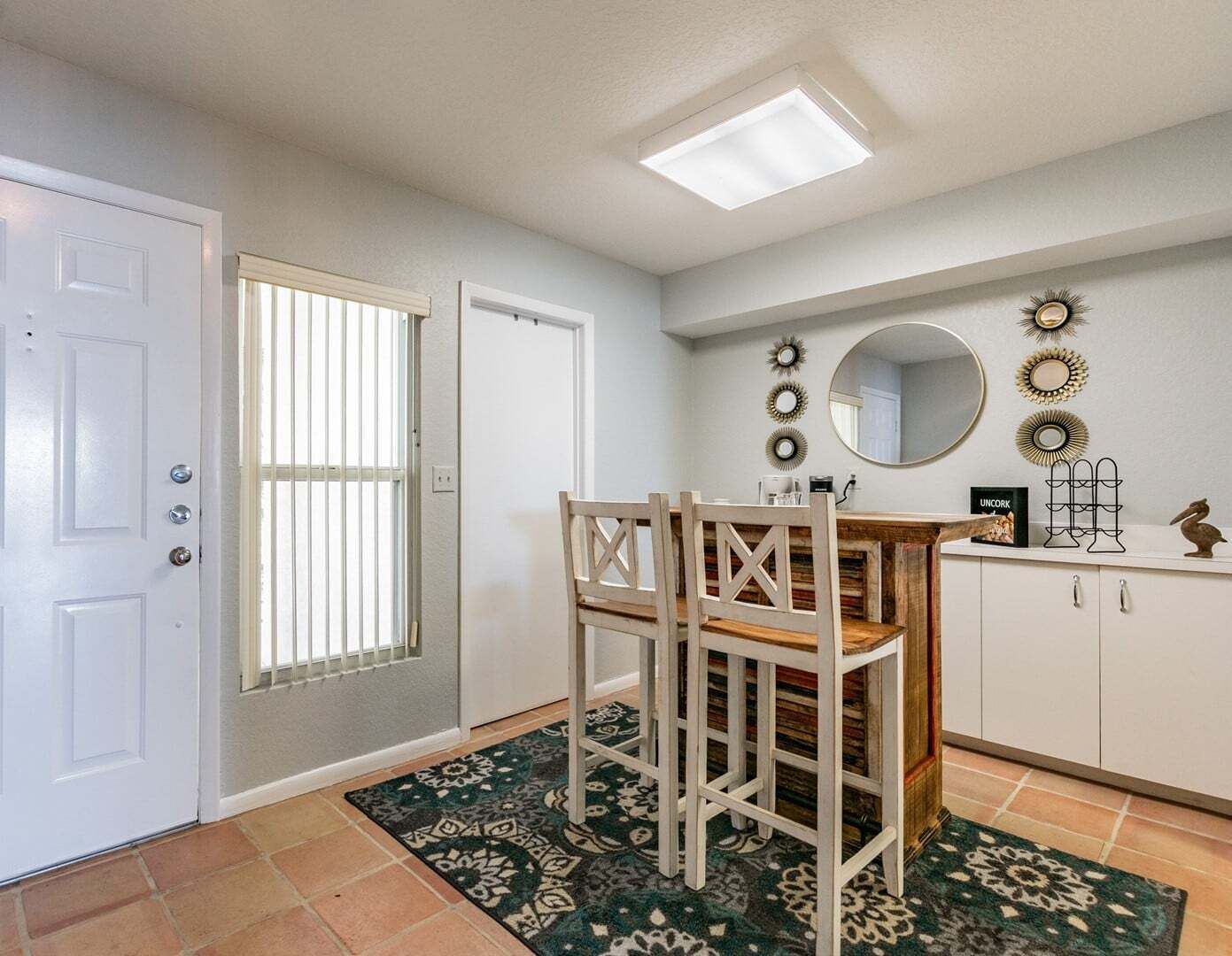 A dining area with a table and chairs, a white door, a window with blinds, and a ceiling light.