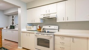 Una cocina con gabinetes blancos, microondas, estufa y cafetera.