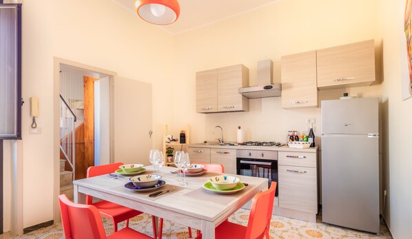Een compacte keuken met een eethoek, met een tafel gedekt voor vier personen, een koelkast en een gasfornuis.