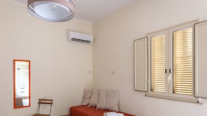 A bedroom with a bed, a chair, a mirror, an air conditioning unit, and a window with blinds. - Violet Guest House (Syracuse)