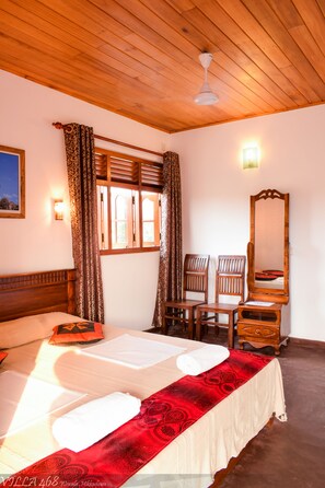 A hotel room with a wooden ceiling, a bed with a red and white bedspread, two wooden chairs, a wooden dresser, and a mirror.