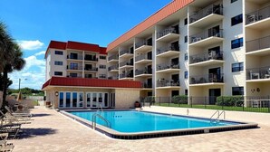 Een meerlaags hotel met een zwembad, balkons en een gebouw met een rood dak.