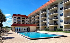 Um hotel de vários andares com piscina, varandas e um edifício com telhado vermelho.