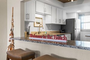 A kitchen with white cabinets, a granite countertop, and a stainless steel refrigerator.
