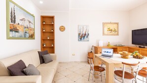 A modern living room with a sofa, a dining table with chairs, a TV, and artwork on the walls.