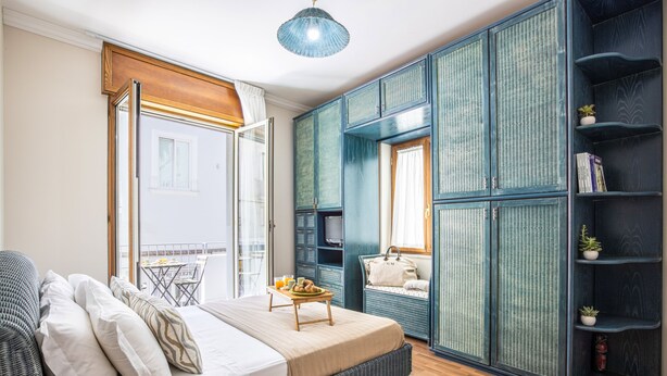 A bedroom with a bed, a small table with breakfast, a wardrobe, and a balcony with a table and chairs.