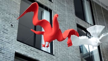 A red and white sculpture of a bird-like creature hanging from a building.