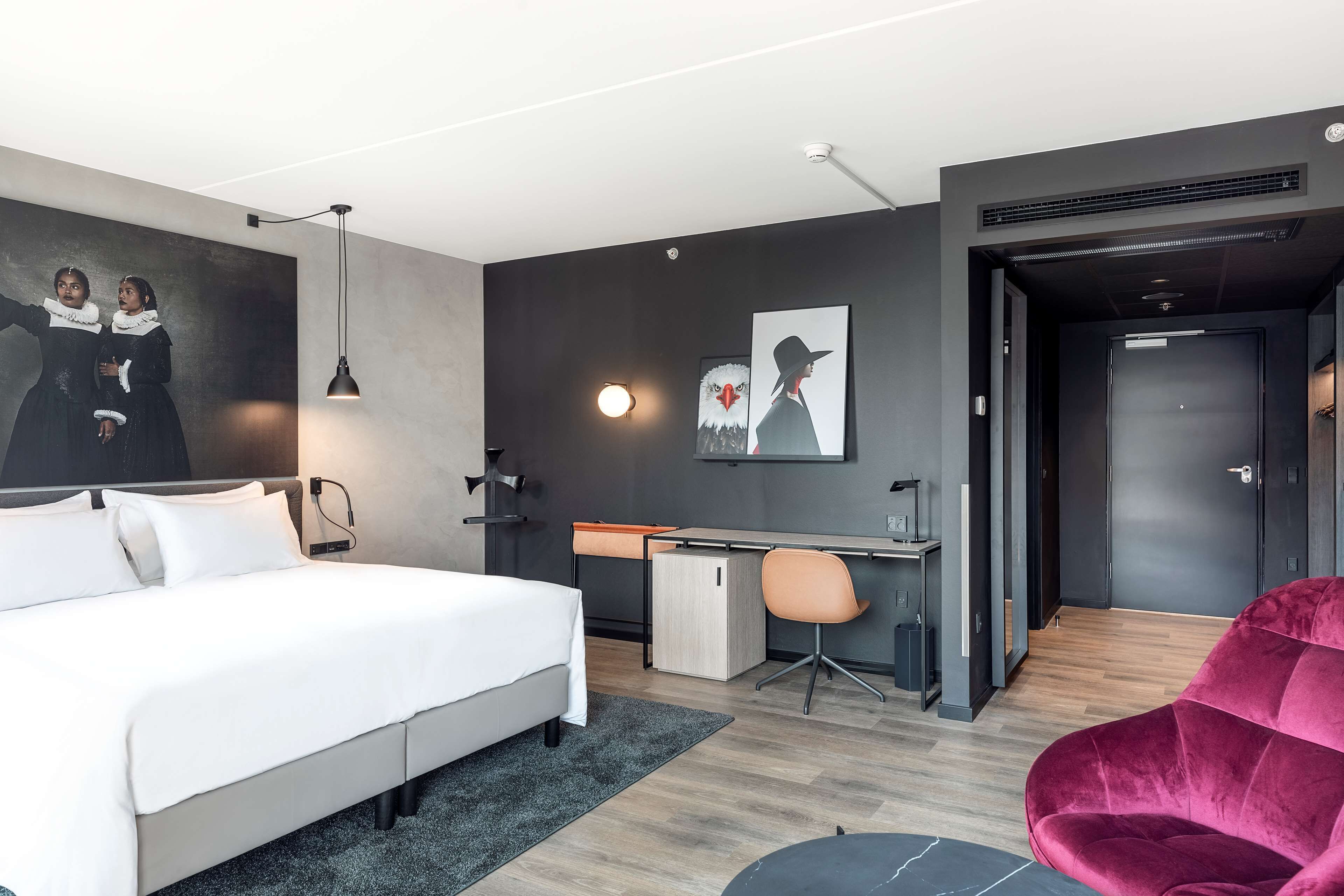 Una habitación de hotel moderna con una cama grande, un escritorio, una silla y obras de arte en las paredes.