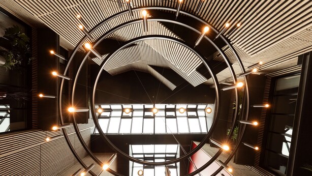 Et moderne interiør med cirkulært design, der viser et centralt åbent rum med udsigt til himlen og vægge med lodrette lister samt hængende lys.