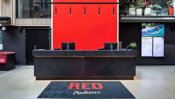 A reception desk with a red accent wall, a black marble countertop, and a black rug with "RED Radissen" text.