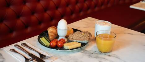 A breakfast setting with croissants, eggs, bread, tomatoes, cheese, and a glass of orange juice on a marble table.