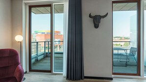 A modern hotel room with a large sliding glass door leading to a balcony, a red chair, and a bull head decoration on the wall.