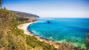 A coastal landscape with a beach, clear blue sea, and boats. - Hotel Cristal Setubal (Setubal)