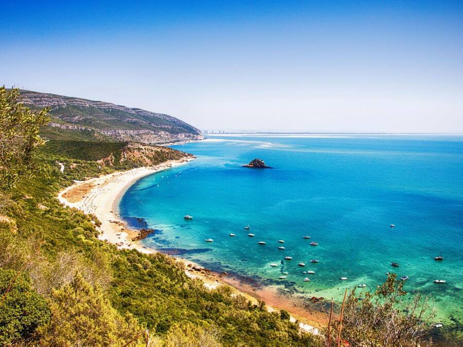 Un paisaje costero con playa, mar azul cristalino y barcos.