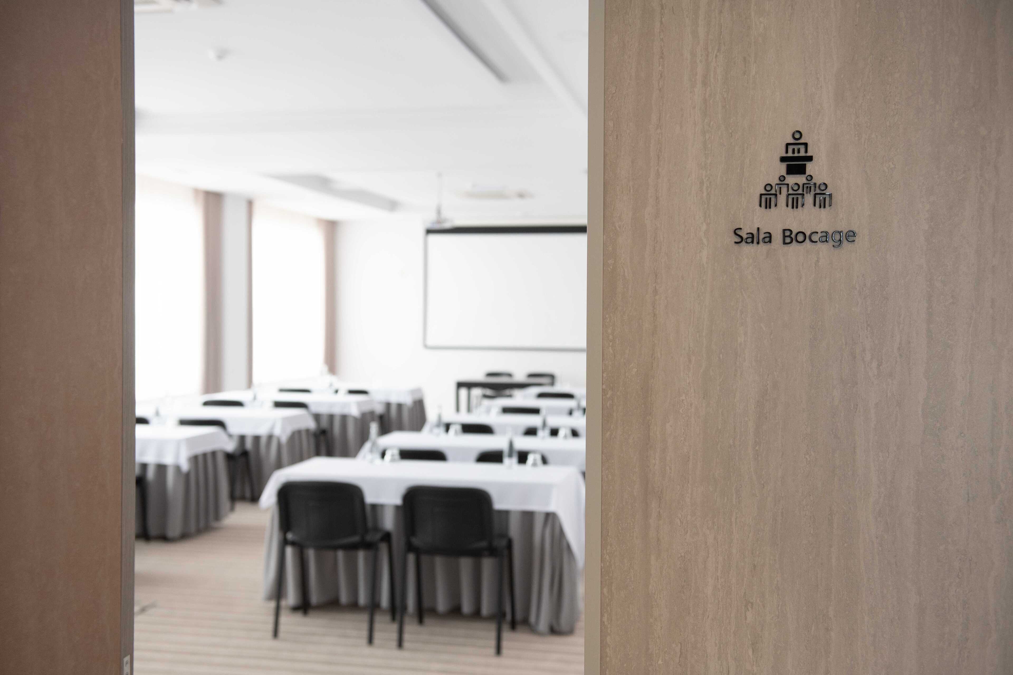 Una sala de conferències amb taules i cadires, una pissarra i el logotip de Sala Bocage.
