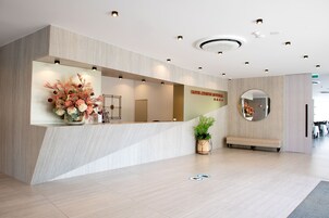 Una moderna zona de recepción con un mostrador de madera, un arreglo floral grande, un espejo y un banco.