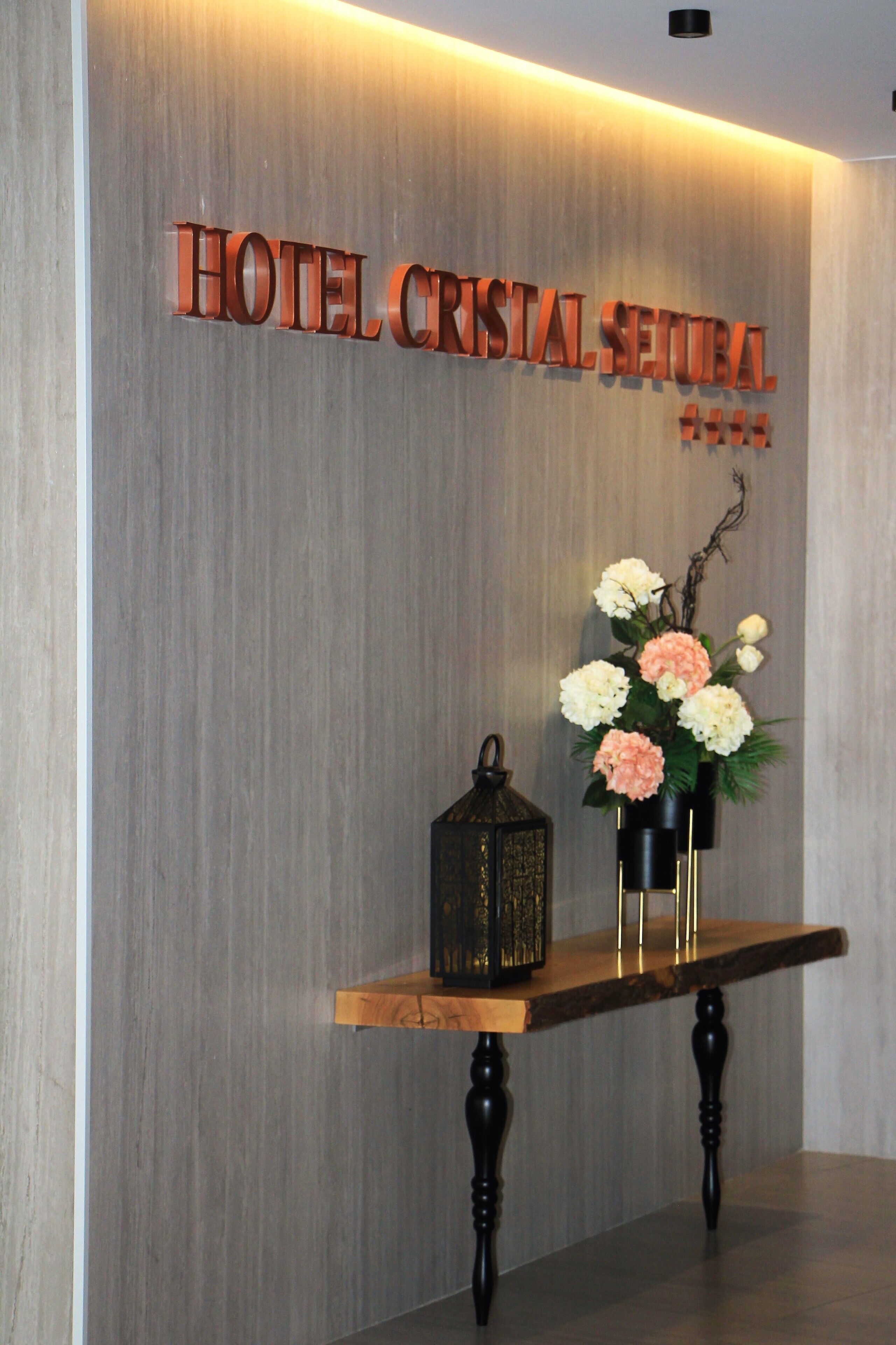 Un comptoir d’accueil avec une enseigne indiquant « HÔTEL CRISTAL SERUMA » et un vase rempli de fleurs.