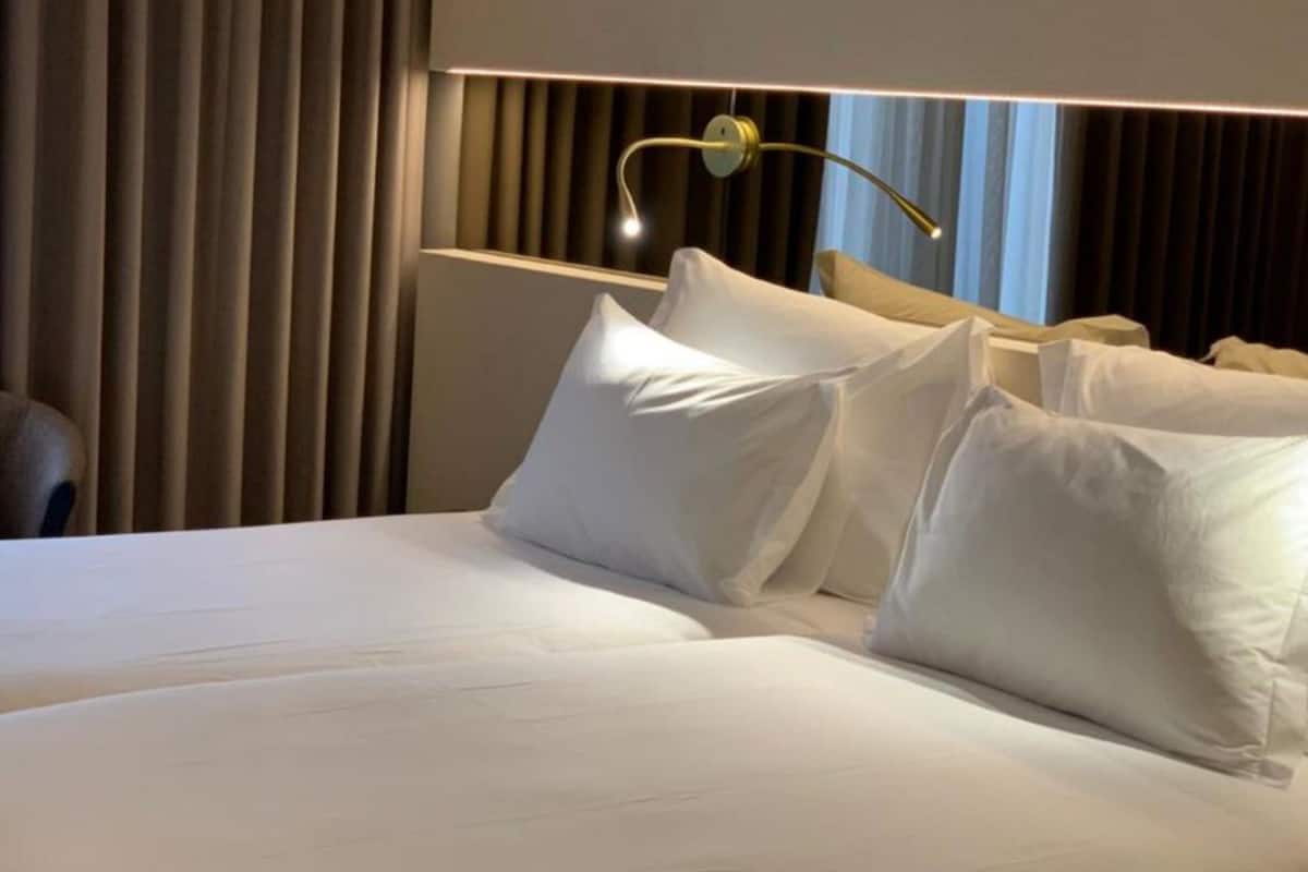A hotel room with a large bed, two pillows, a bedside table, and a lamp.