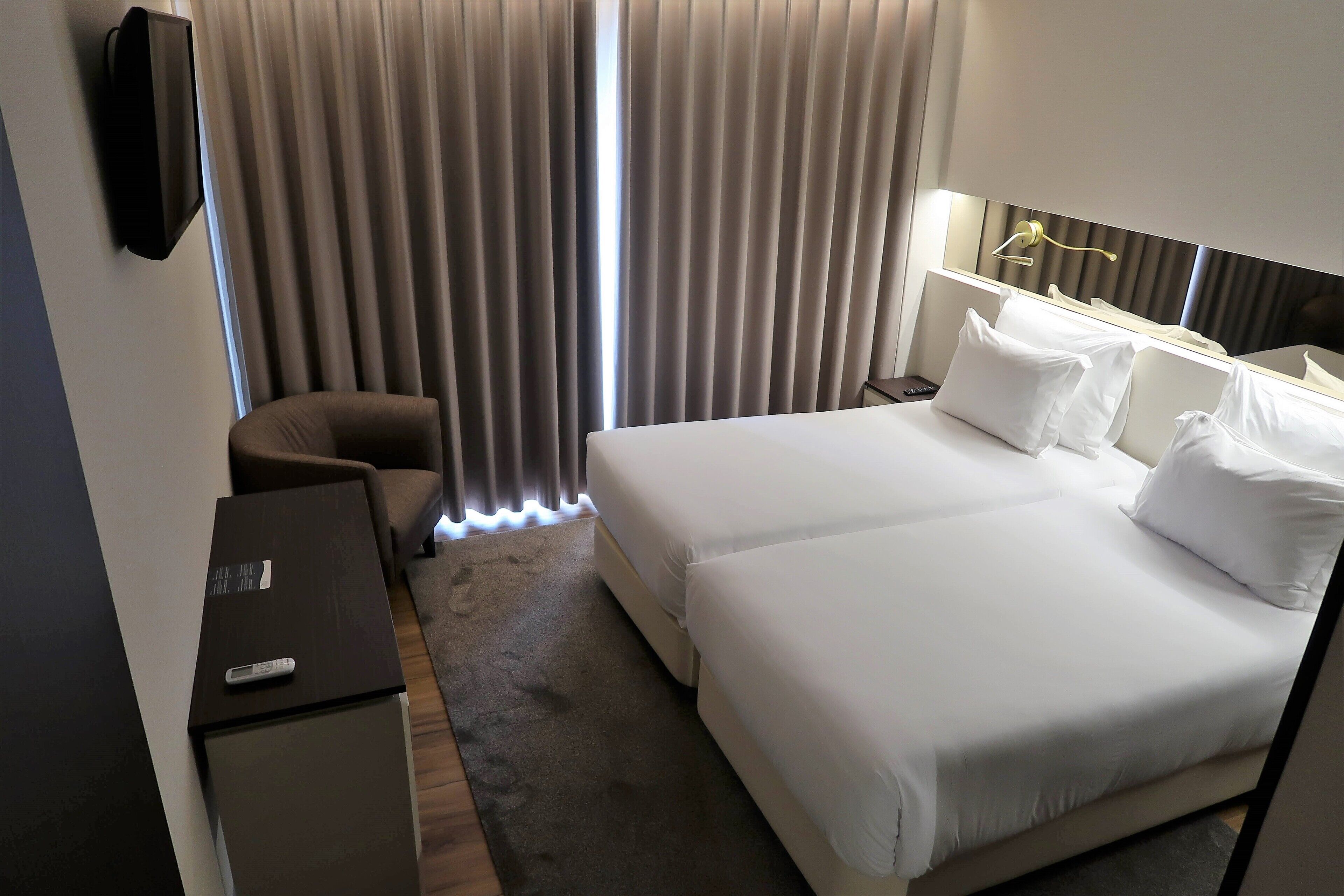 A hotel room with a bed, a desk, a chair, and a TV.