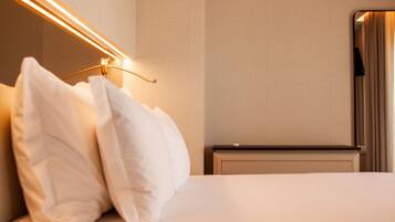 A neatly made bed with white linens and pillows, a bedside table, a lamp, and a mirror on the wall.