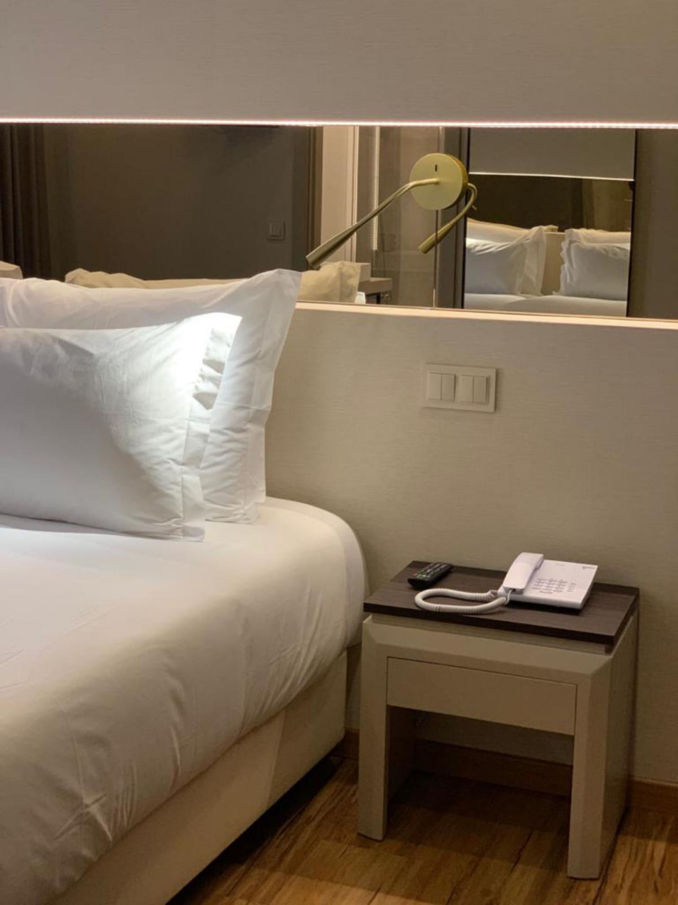 Una habitación de hotel con una cama, una mesita de noche con un teléfono y un espejo que refleja la cama.
