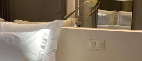 Una habitación de hotel con una cama, una mesita de noche con un teléfono y un espejo que refleja la cama.