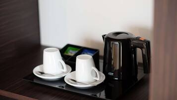 A coffee station with a black coffee maker, two white cups, and a spoon on a tray.