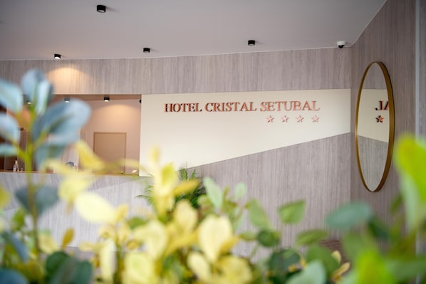 A reception area with a sign for HOTEL CRISTAL SETUBAL, a mirror, and some indoor plants.