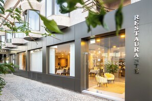 A modern restaurant with a glass facade, interior seating, and a visible outdoor seating area.