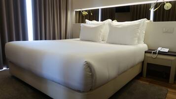 A neatly made bed with white linens, a bedside table with a phone, and a wall-mounted light fixture.