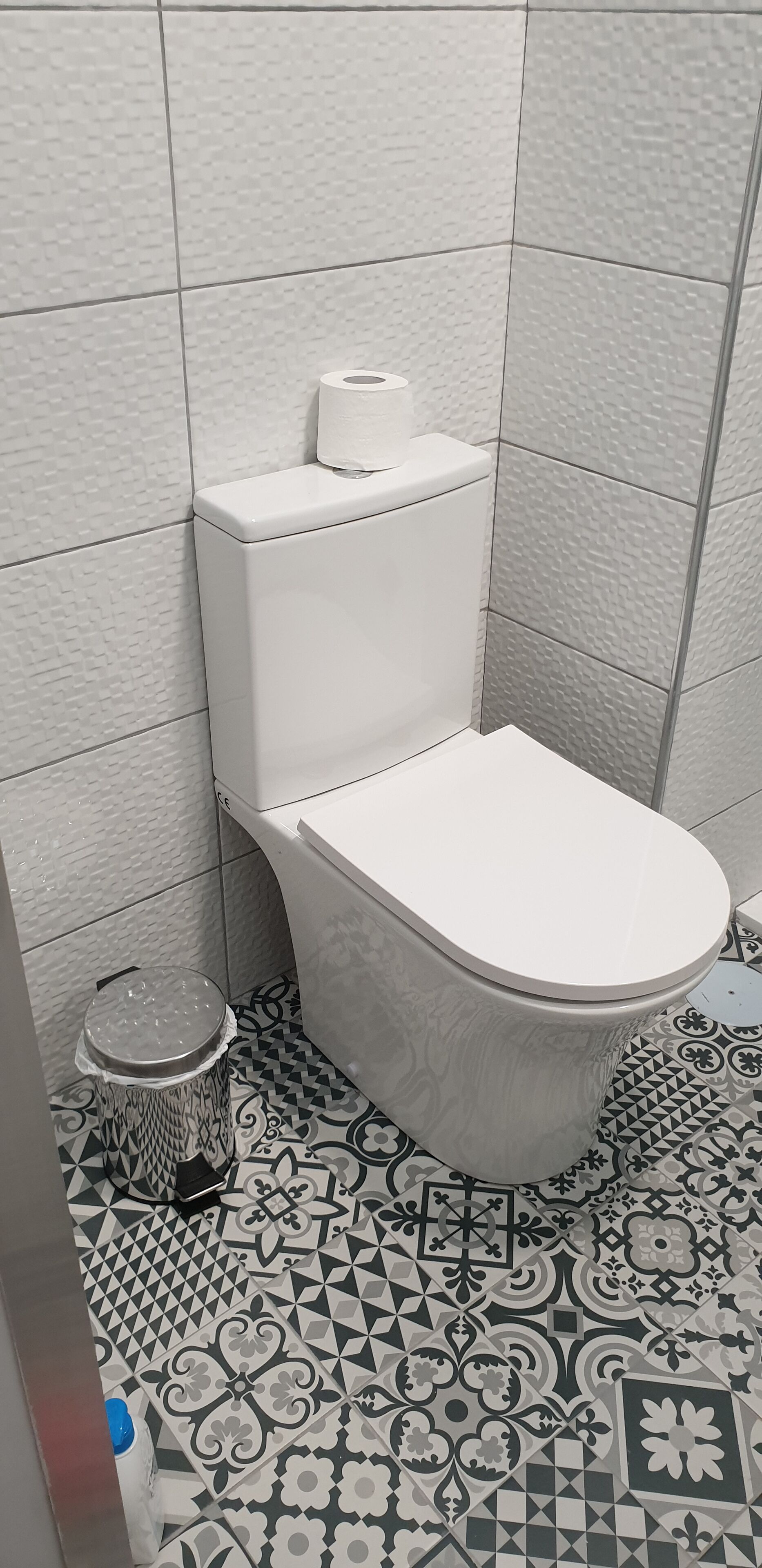 Un baño con inodoro, baldosas de piso estampadas y un cesto de basura.