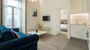 A modern living room with a sofa, a coffee table, and a TV. There is a kitchen area with a sink and cabinets. - Morgan-Jupiter Apartments (Lisbon)