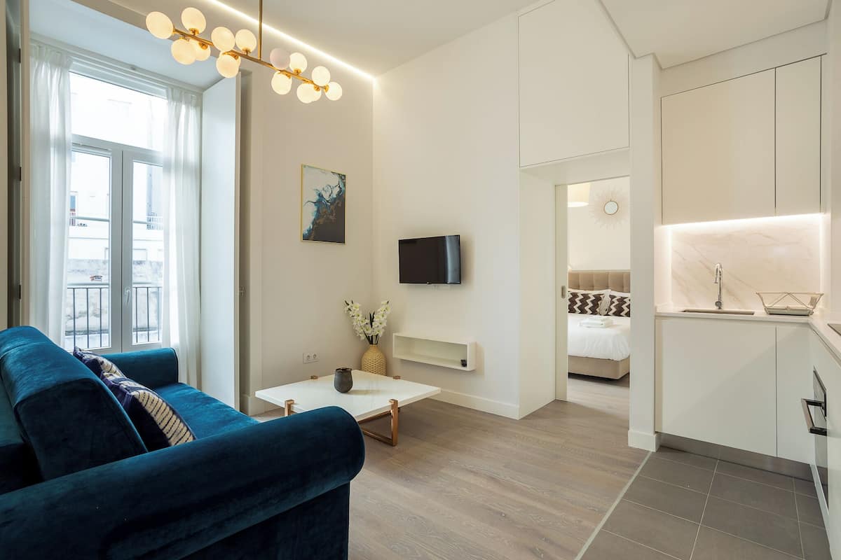 A modern living room with a sofa, a coffee table, and a TV. There is a kitchen area with a sink and cabinets.