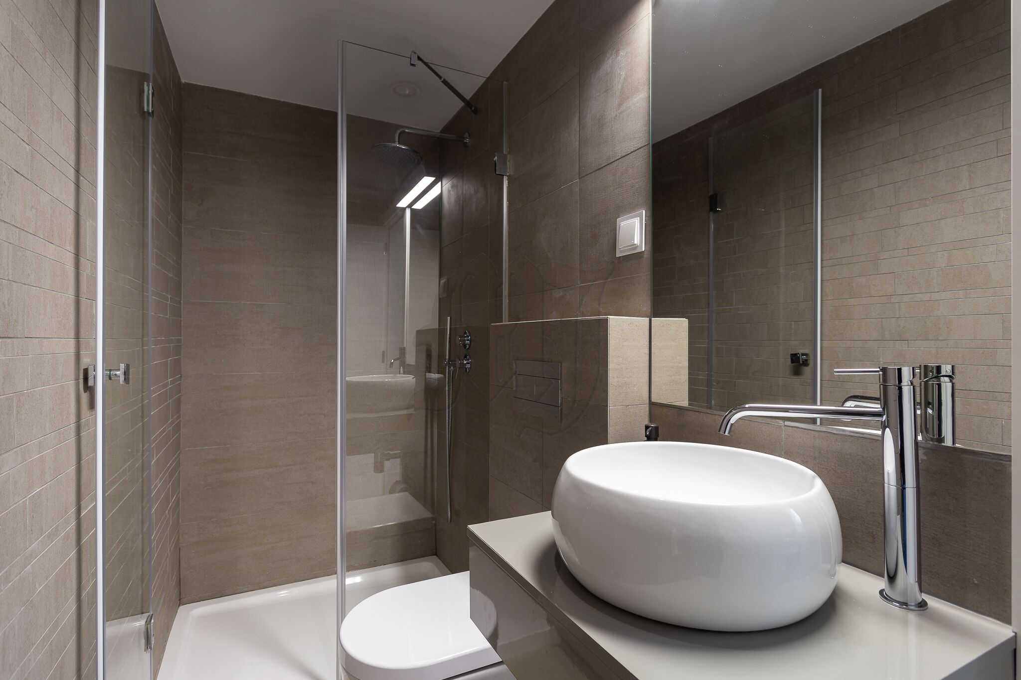 A modern bathroom with a glass-enclosed shower, a white sink, and a toilet.