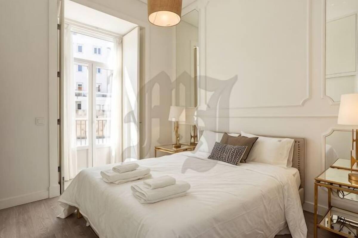 A hotel room with a large bed, bedside tables, a mirror, and a view of the outside.