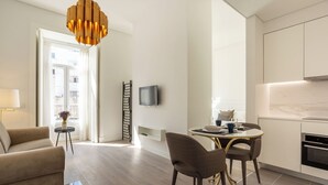 A modern living room with a sofa, a dining table with chairs, a TV mounted on the wall, and a kitchen area with cabinets and a stove. - Morgan-Jupiter Apartments (Lisbon)