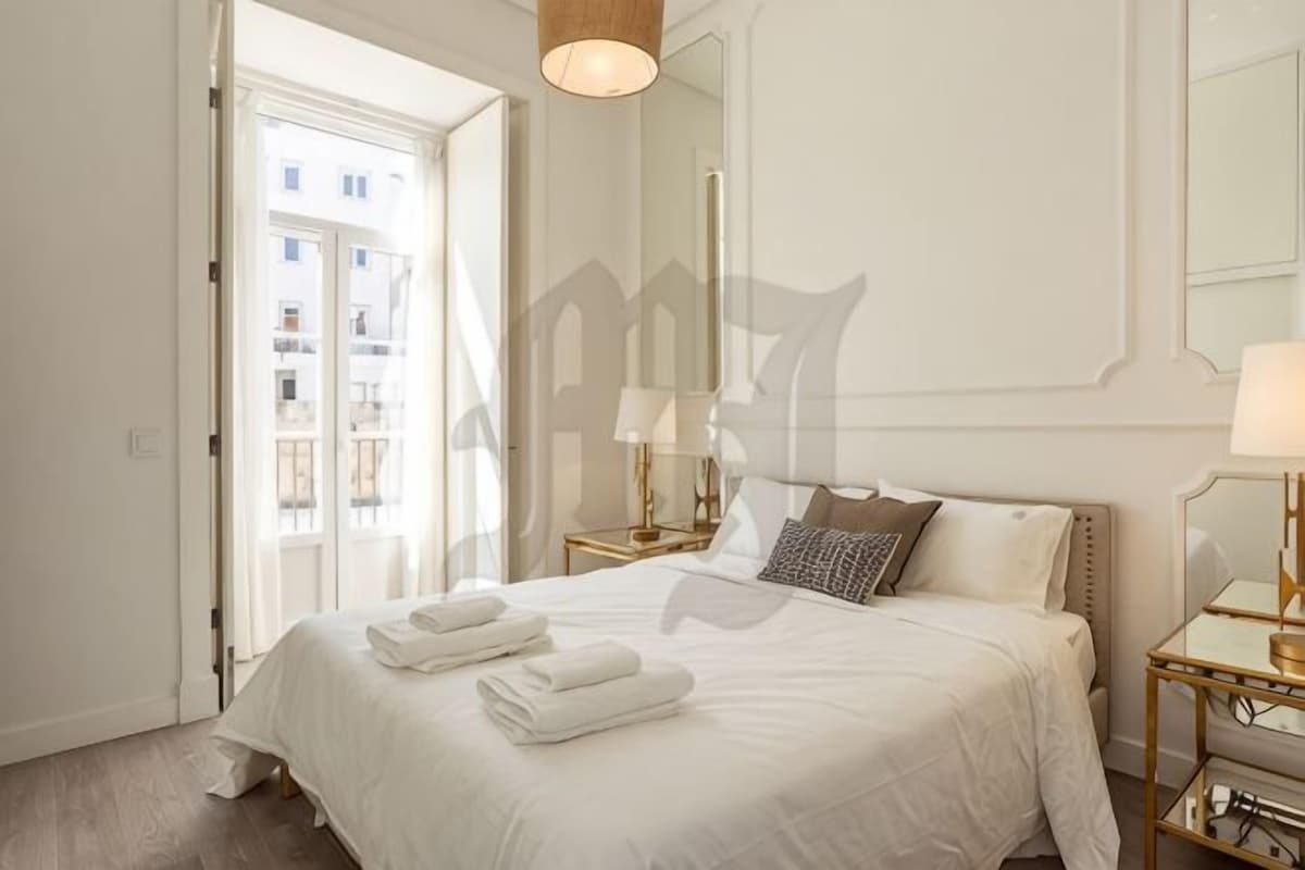 A hotel room with a large bed, bedside tables, a mirror, and a view of the outside.