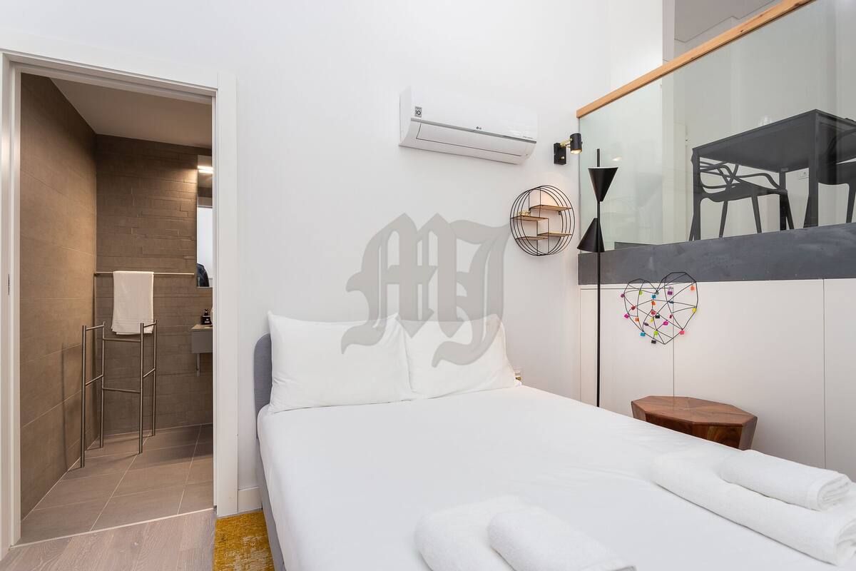A modern hotel room with a bed, a towel rack, an air conditioner, and a mirror reflecting a dining area.
