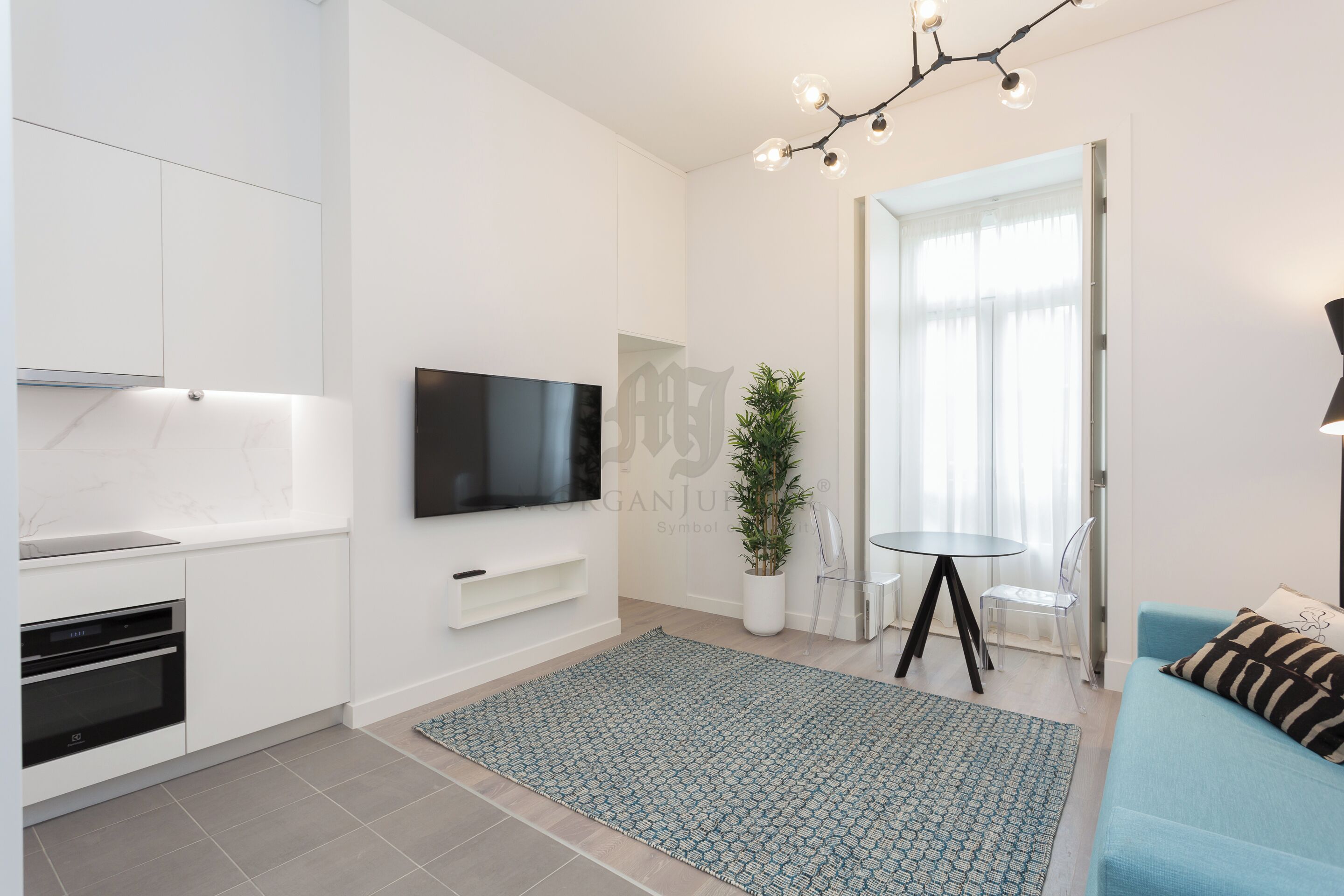 A modern living room with a flat-screen TV, a dining area with a small table and chairs, a sofa, and a potted plant.