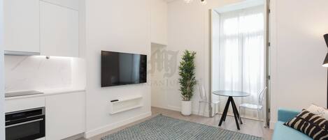 A modern living room with a flat-screen TV, a dining area with a small table and chairs, a sofa, and a potted plant.