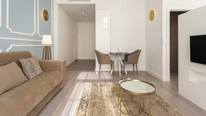 A modern living room with a sofa, a coffee table, a dining area with chairs, and a TV mounted on the wall. - Morgan-Jupiter Apartments (Lisbon)